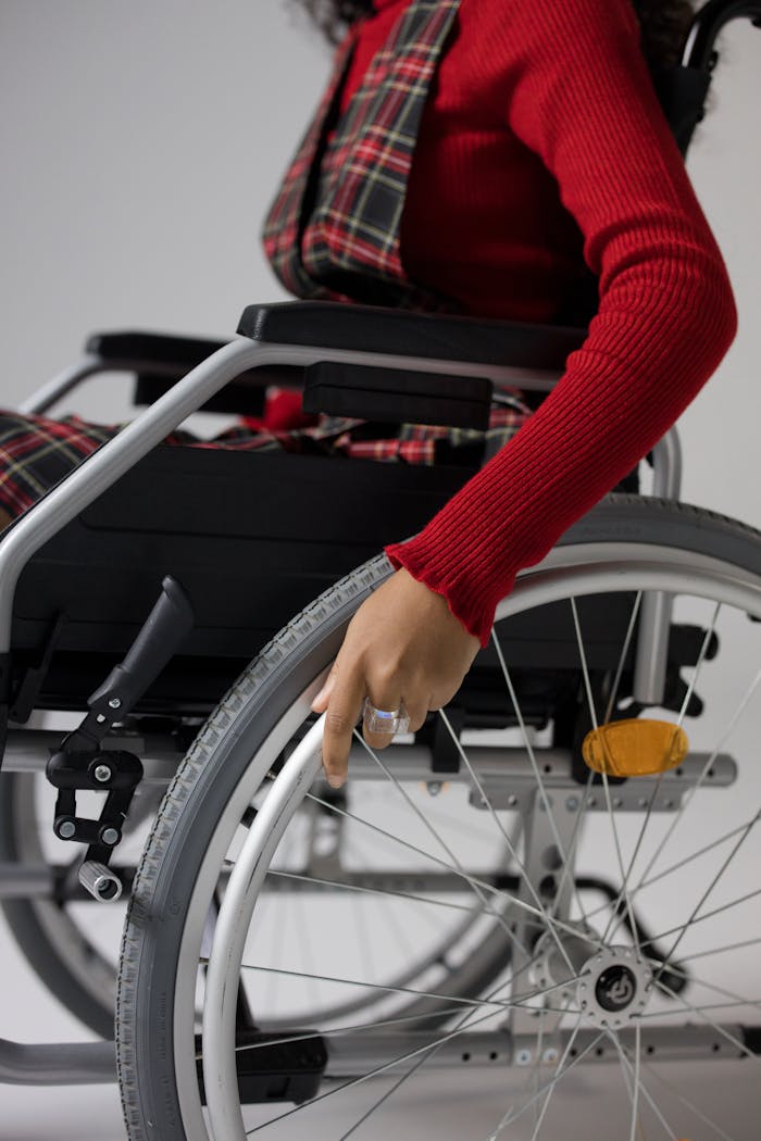 Close-up of a woman in a red sweater and plaid overalls maneuvering a wheelchair indoors.